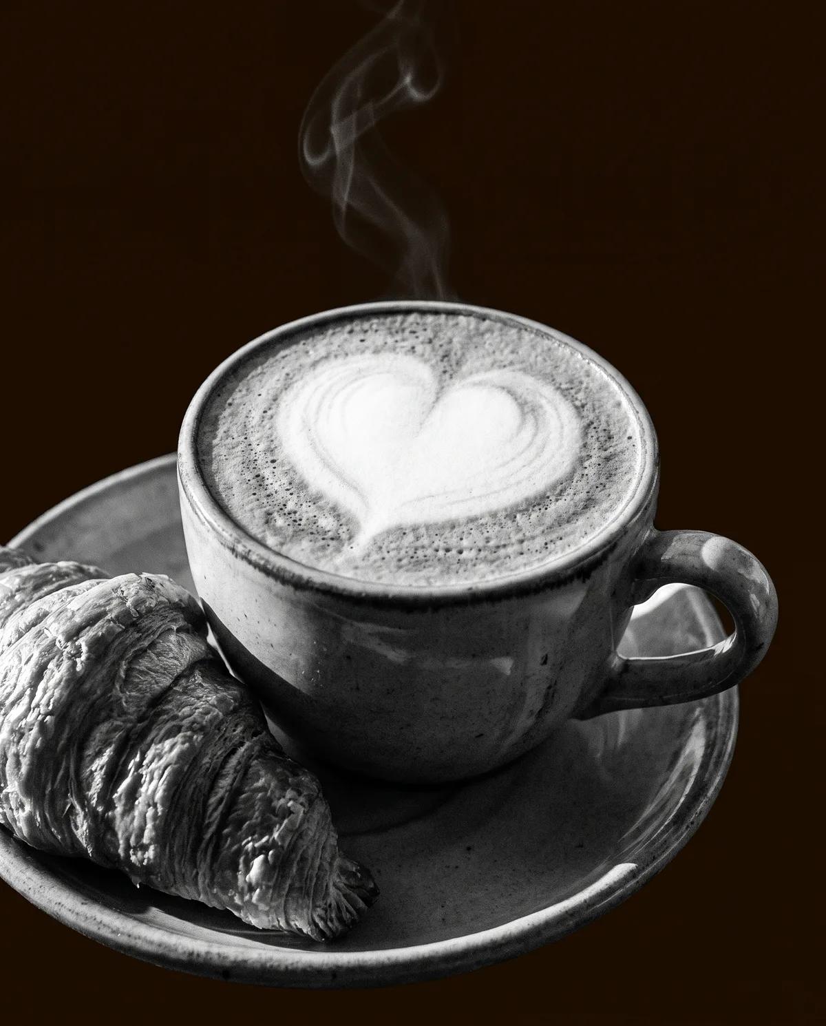 Cappuccino con un cuore nella schiuma e un cornetto dorato.